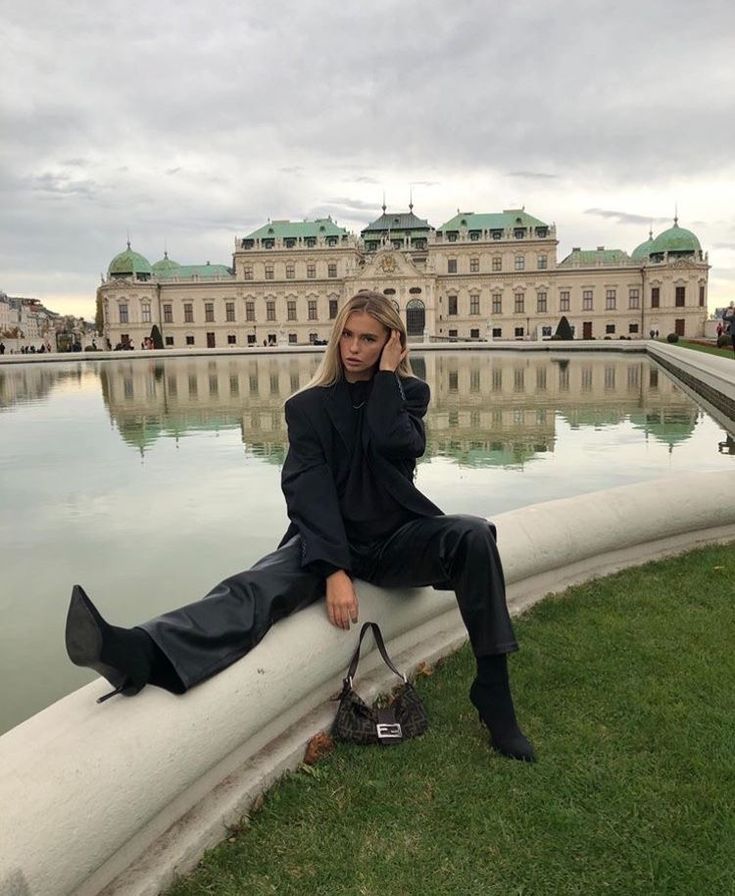 a woman sitting on the edge of a pond talking on her cell phone while holding a purse