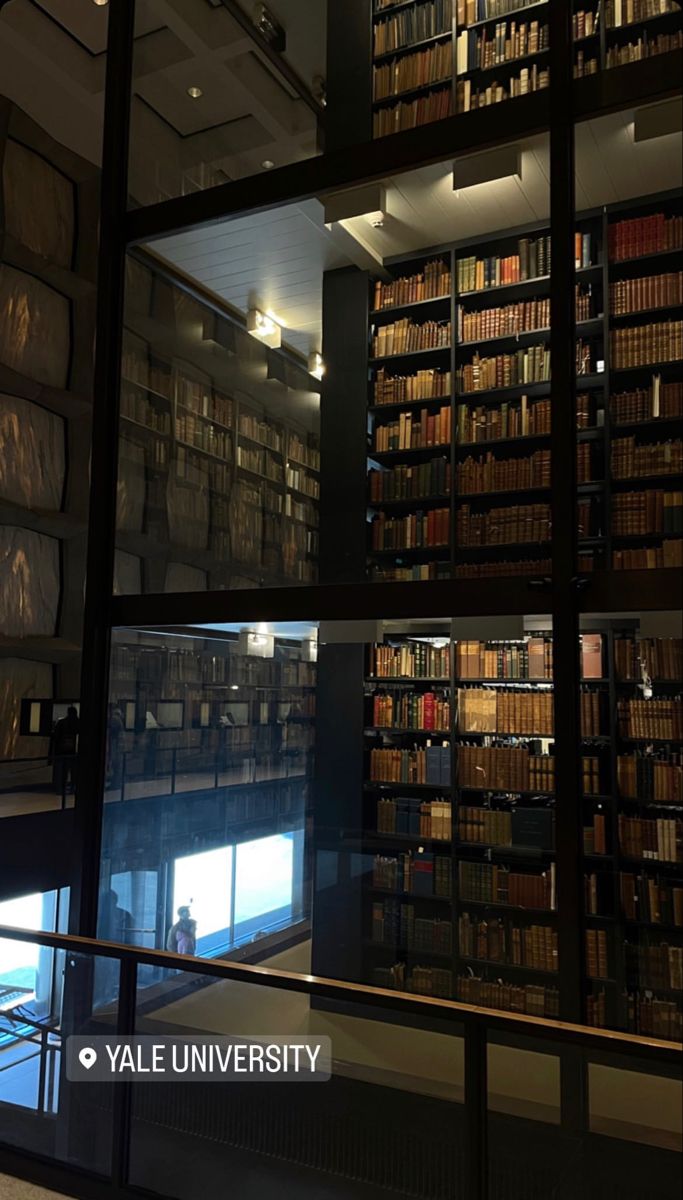 a library filled with lots of books next to a tall glass wall full of books