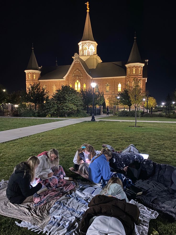 some people are laying on the grass in front of a large building with a clock tower