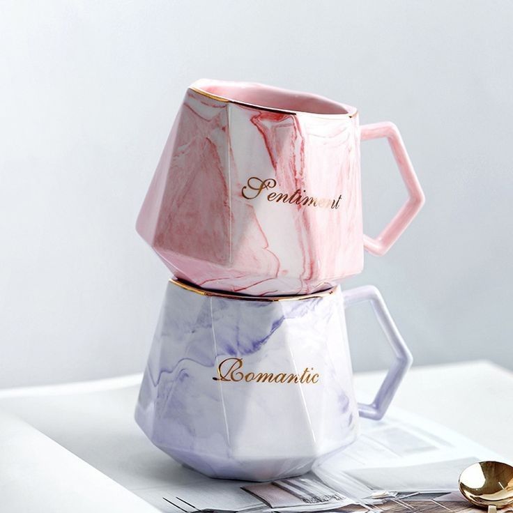 two marbled coffee mugs sitting on top of each other next to a spoon