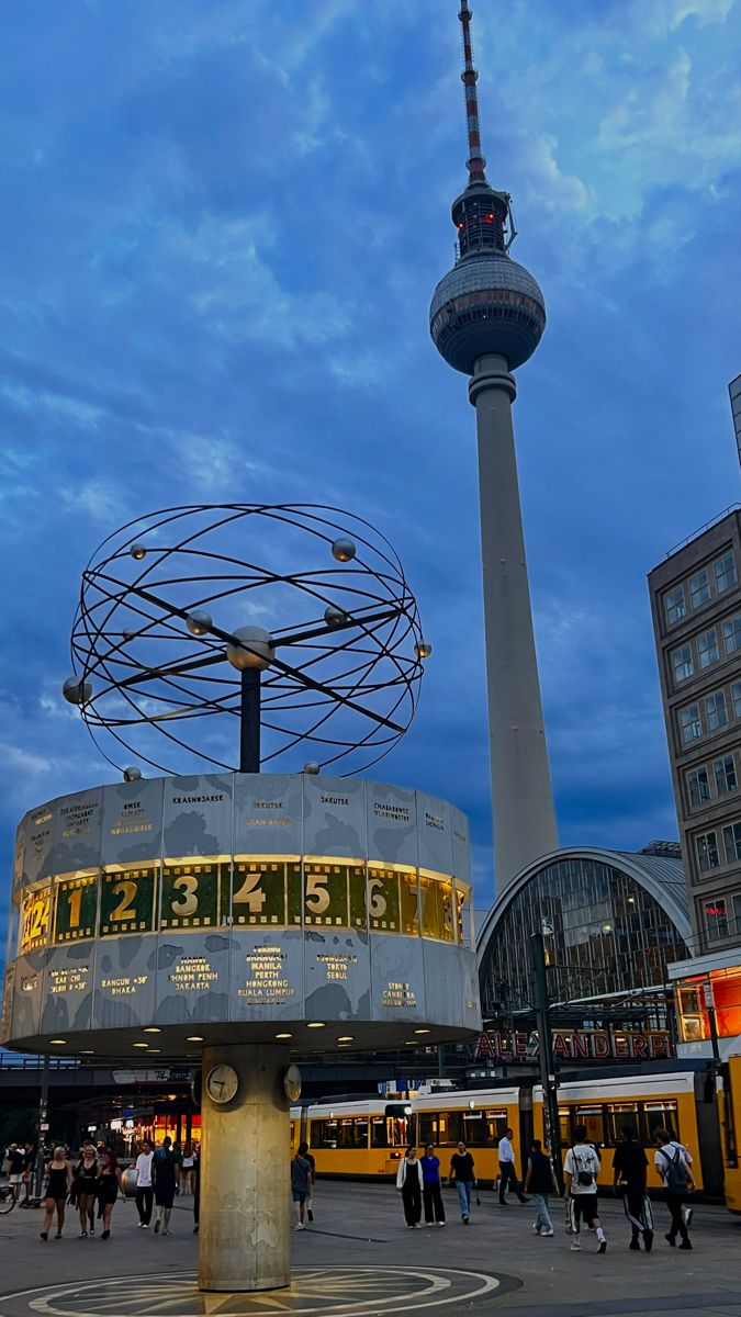 people are walking around in front of a building with a television antenna on top and a clock tower behind it