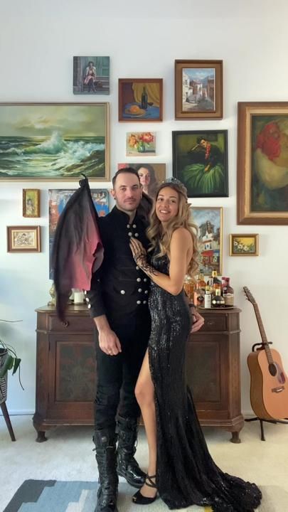 a man and woman posing for a photo in front of paintings on the wall behind them