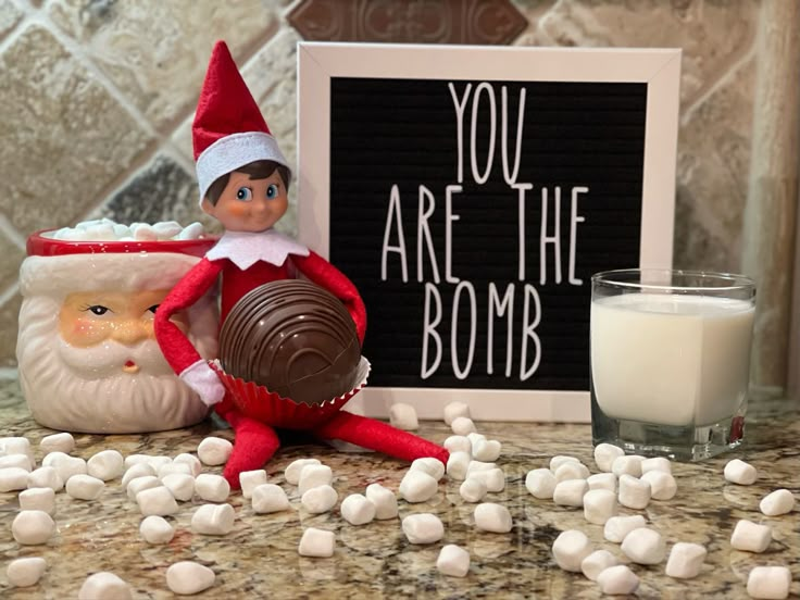 an elf is sitting next to marshmallows and a sign that says you are the bomb