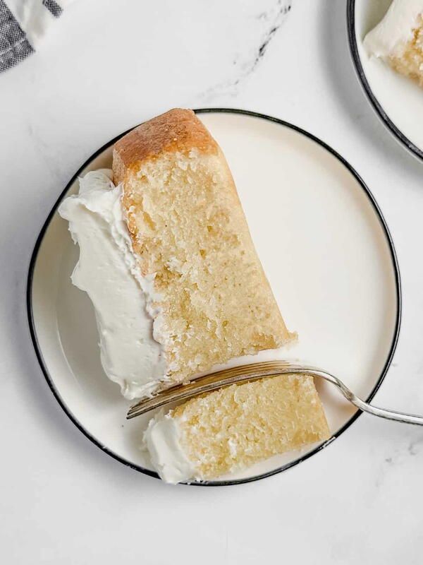 a slice of white cake on a plate with a fork next to the rest of the cake