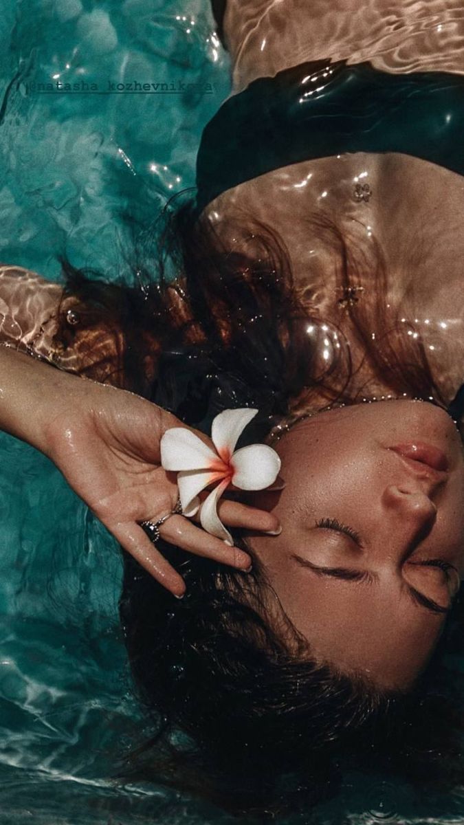 a woman laying in the water with a flower on her head and hands over her face