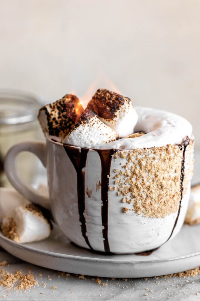 a cup filled with hot chocolate and marshmallows on top of a plate