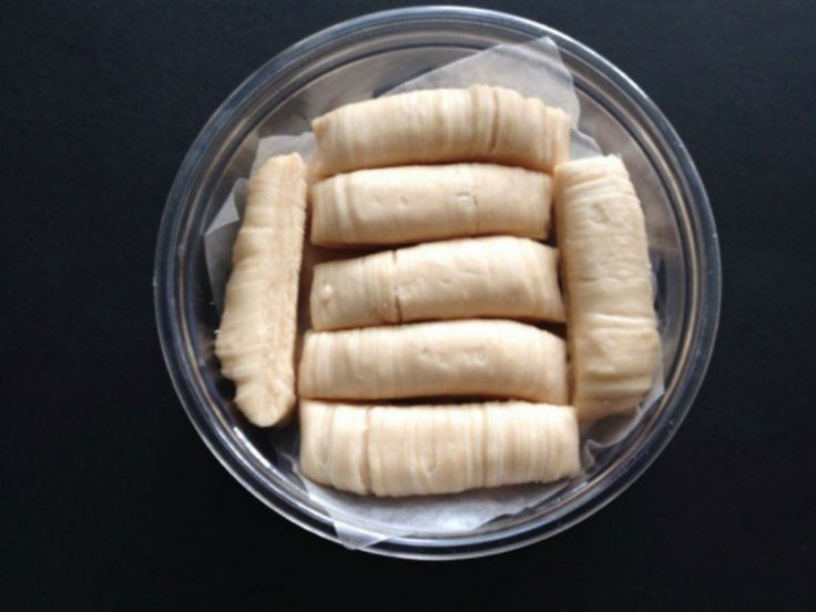 peeled bananas in a plastic container on a black table top with white wax paper around them