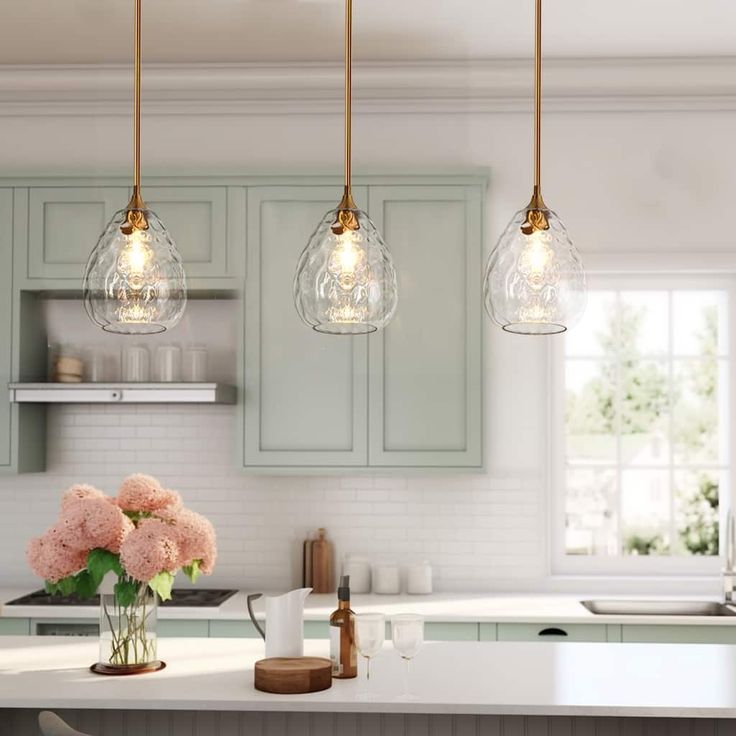 three lights hanging over a kitchen island with flowers in vases on the counter top