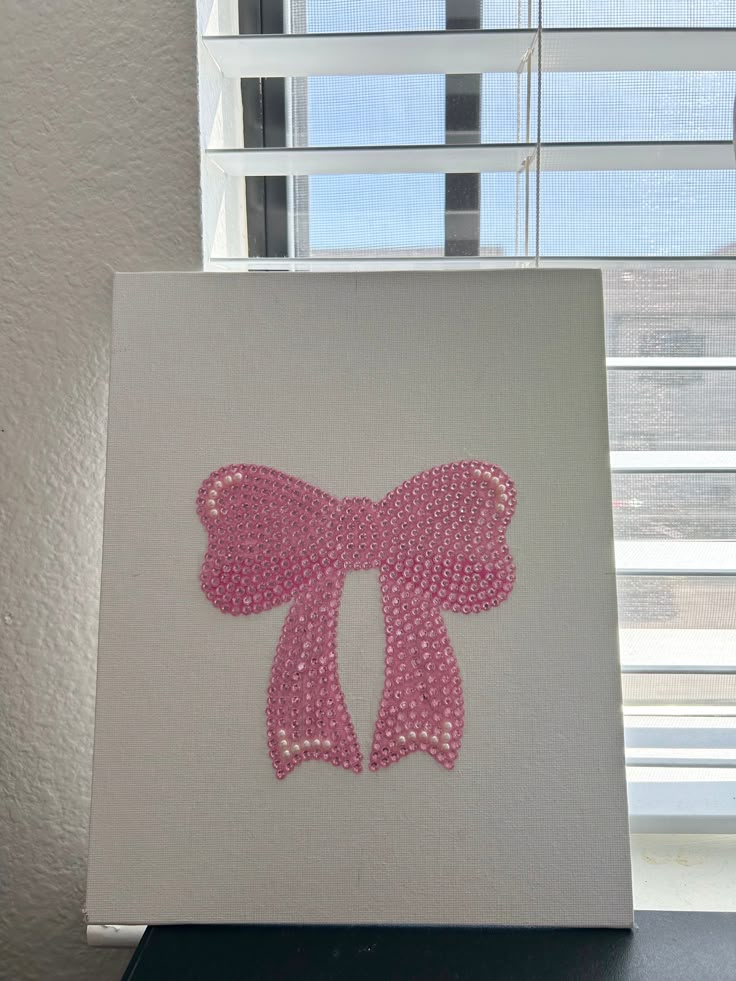 a canvas with a pink bow on it in front of a window