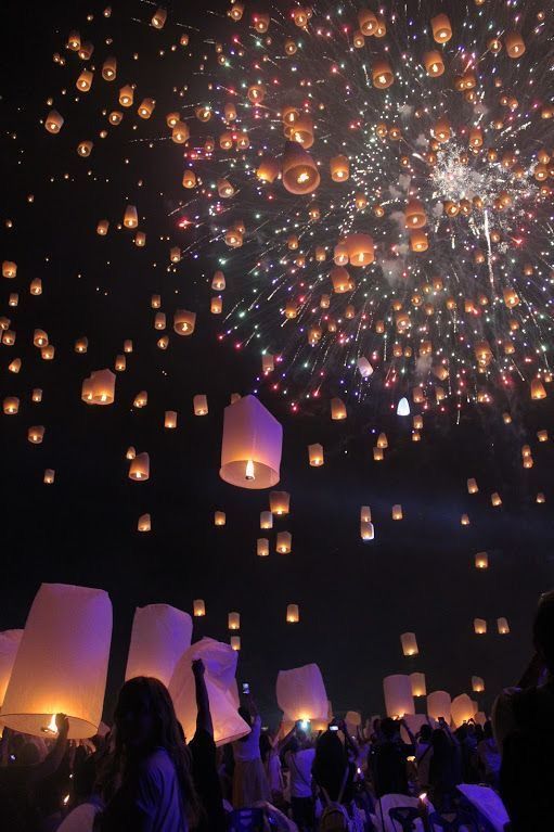 many people are flying paper lanterns in the night sky with lights on them as well