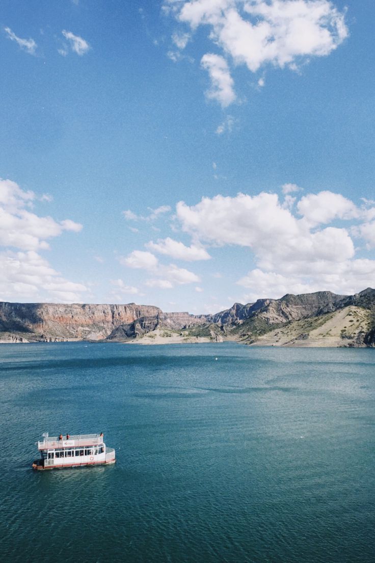 a boat floating on top of a large body of water under a cloudy blue sky