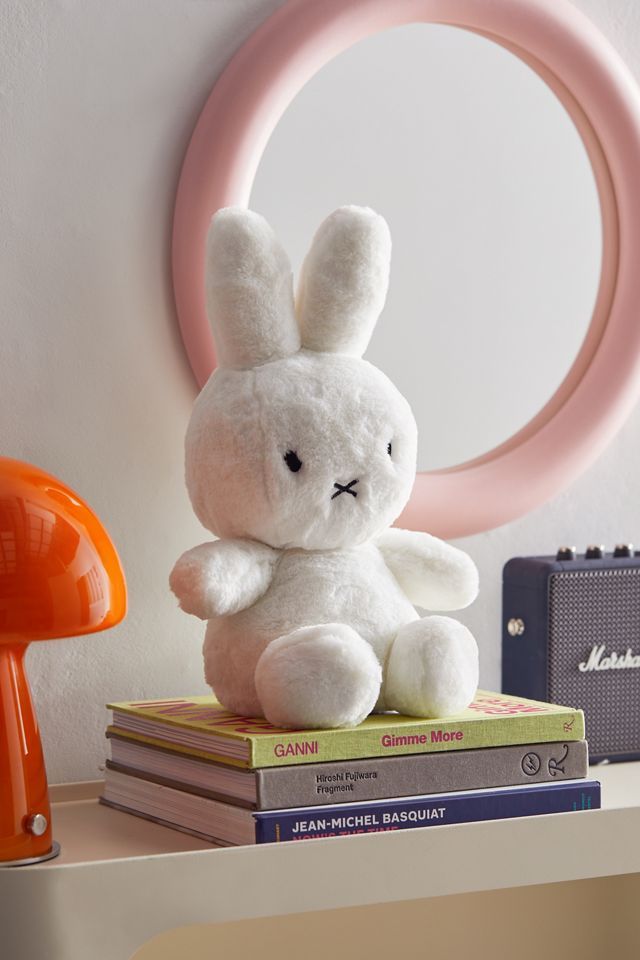 a white stuffed rabbit sitting on top of books in front of a pink circle frame