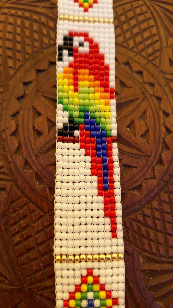 a beaded bracelet with a colorful parrot design on it's side, sitting on top of a wooden table