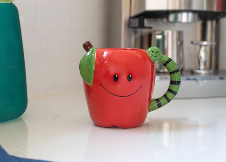 a red apple with a green leaf on it sitting next to a blue vase filled with water