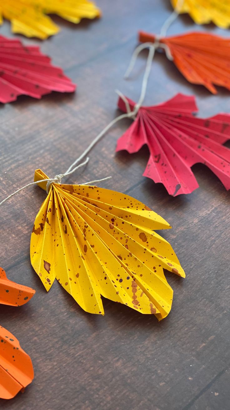 colorful paper leaves are laid out on a wooden surface with string attached to the strings