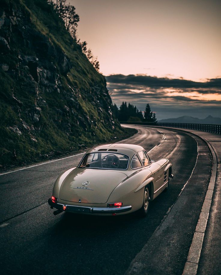 an old car is driving down the road at sunset or dawn in the country side