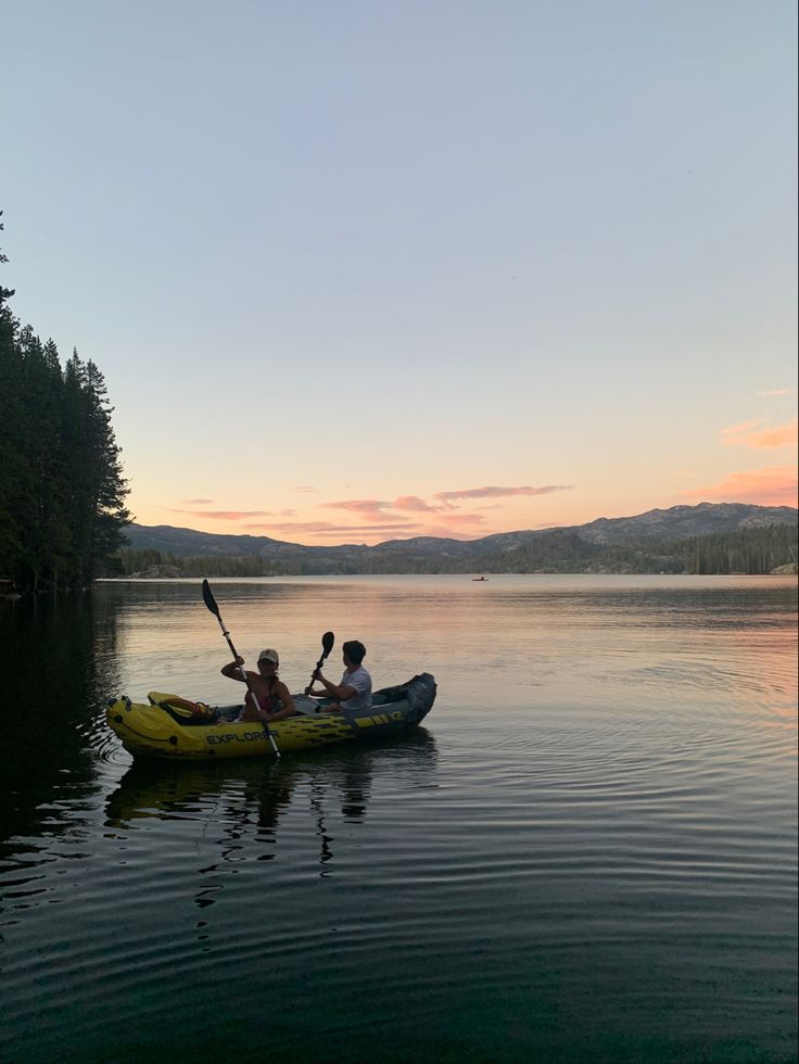 two people in a kayak paddling on the water at sunset with mountains in the background