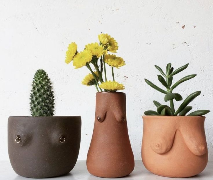 three clay vases with flowers in them on a white countertop next to a cell phone