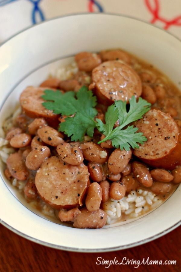 a white bowl filled with beans and sausage on top of rice next to a green leafy garnish