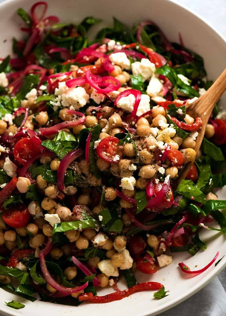 a white bowl filled with salad topped with red onions and feta cheese on top