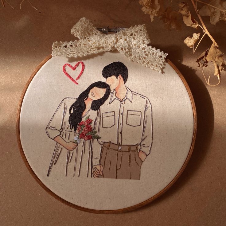 an embroidered picture of a man and woman with a heart on their forehead, next to some dried flowers