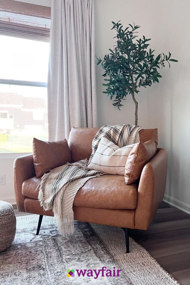 a living room with a couch, chair and potted tree in the window sill