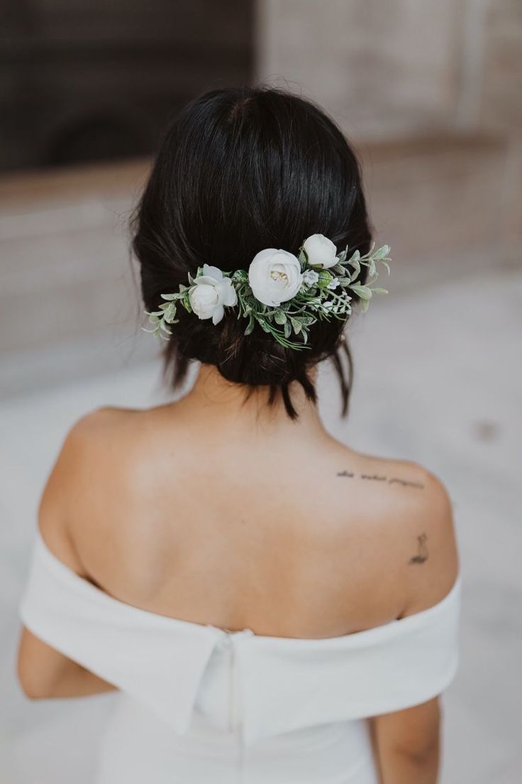 a woman wearing a white dress with flowers in her hair and a tattoo on her shoulder