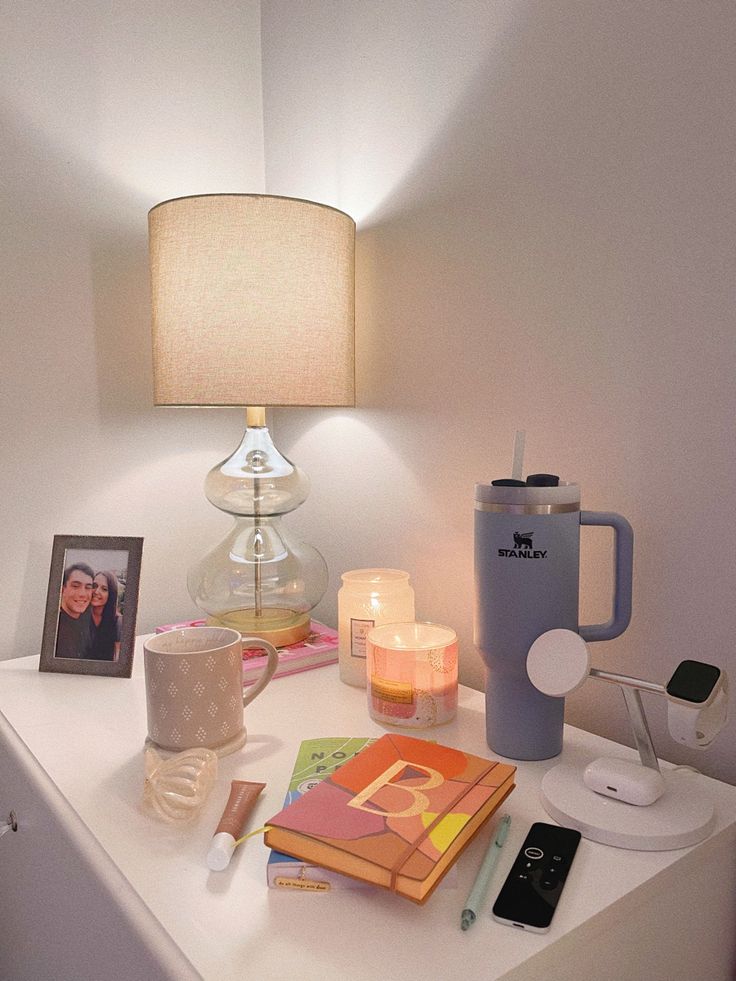 a white table topped with a lamp next to a cup and book on top of it