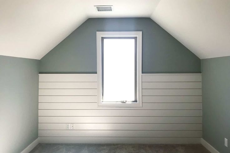 an empty room with gray walls and white paneling on the wall, along with a window