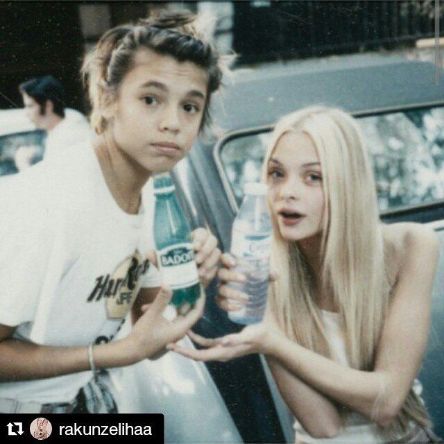 two people standing next to each other near a car and one is holding a bottle