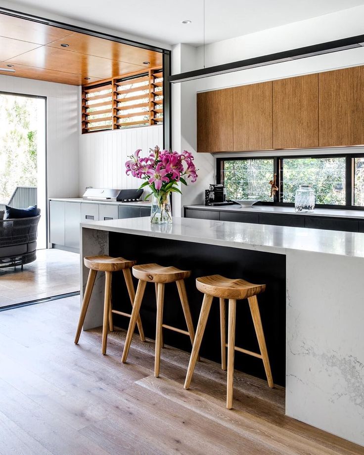 two stools in front of an island with flowers on the counter and windows behind it