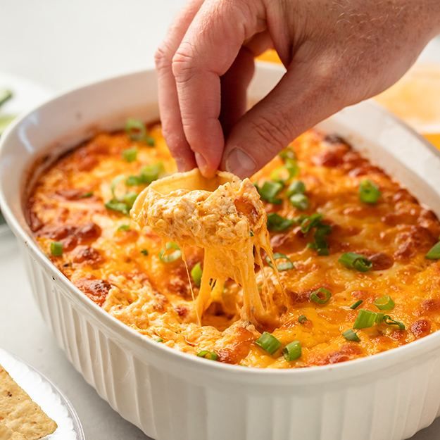 a person dipping cheese into a casserole dish