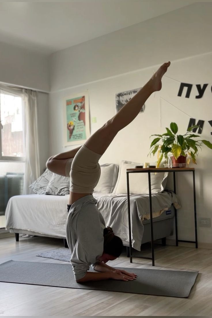 a woman doing a handstand on a yoga mat in front of a bed