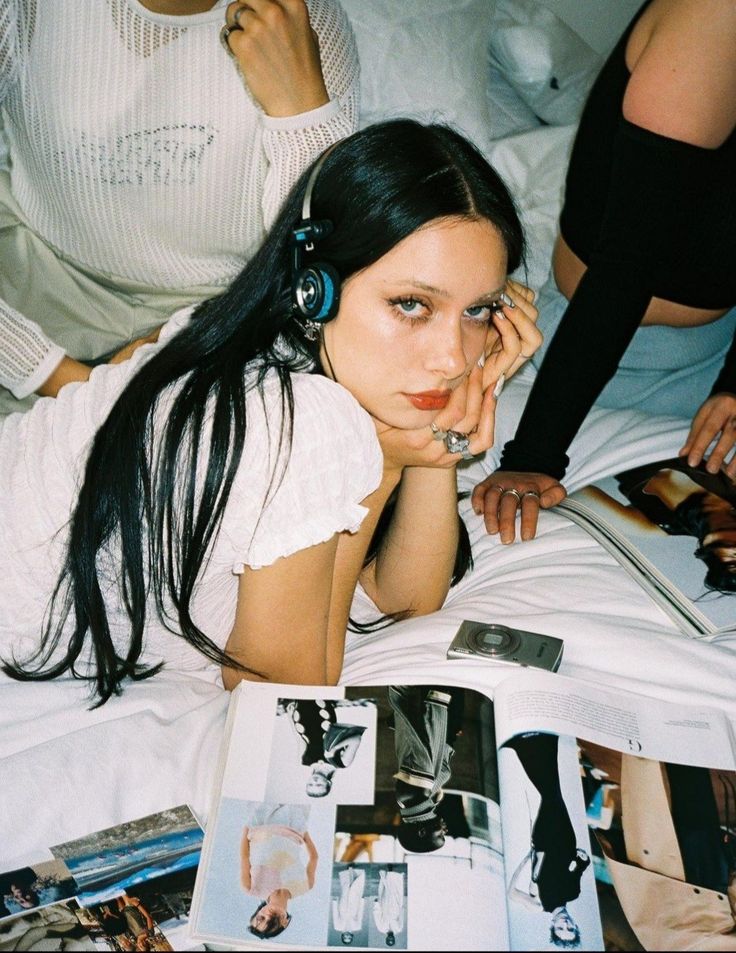 a woman laying on top of a bed with headphones in her ears next to magazines