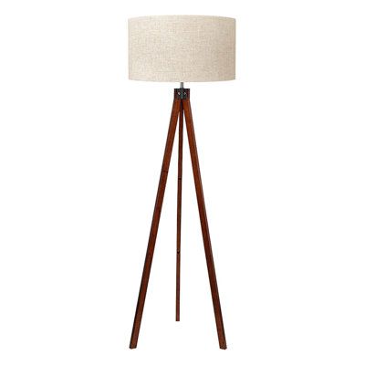 a wooden tripod floor lamp with a white linen shade on the top and brown legs