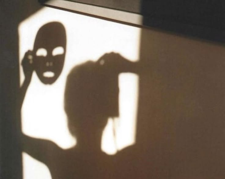 the shadow of a person with a mask on their face is cast onto a wall