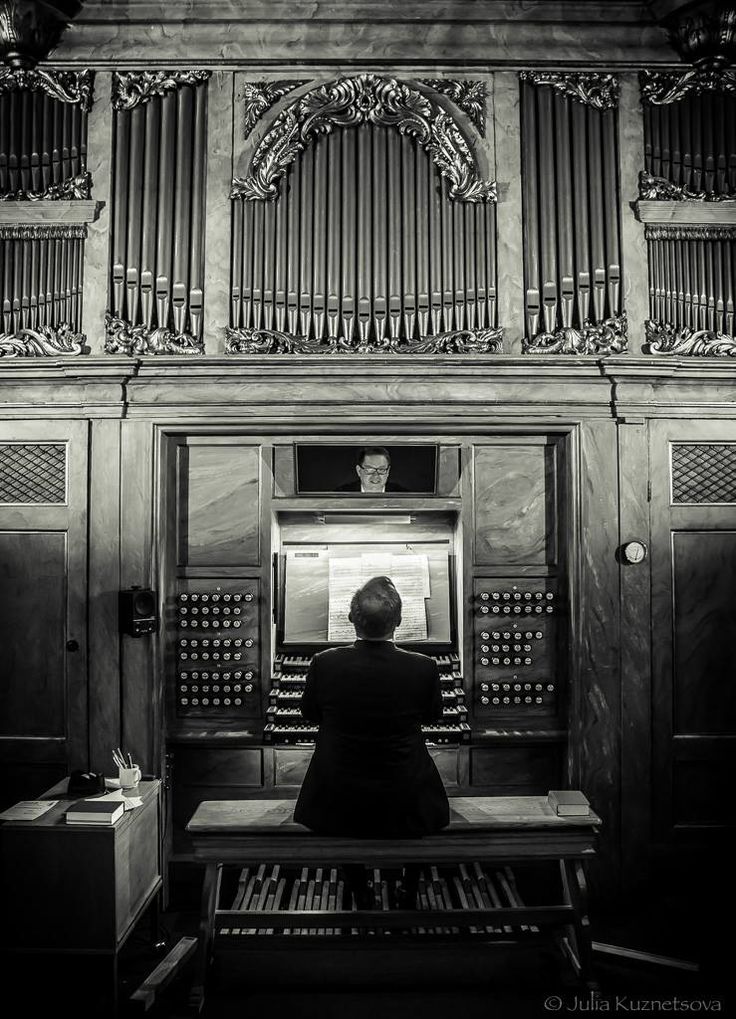 a person sitting on a bench in front of a pipe organ and looking at the screen