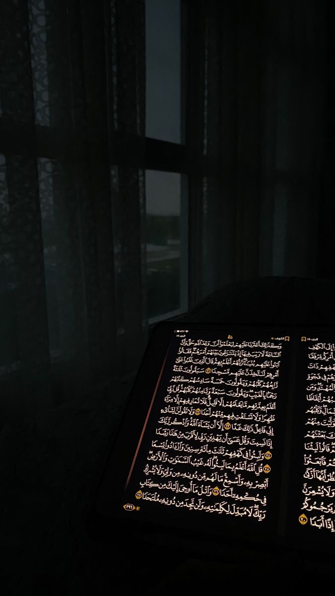 an illuminated book in the dark with arabic writing on it's cover and window behind it