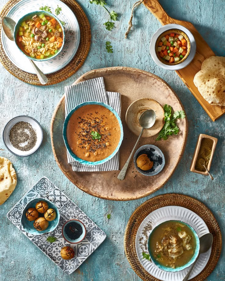 bowls of soup and bread sit on a blue tablecloth, with spoons in each bowl