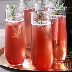 four glasses filled with wine and garnished with rosemary sprigs on a tray