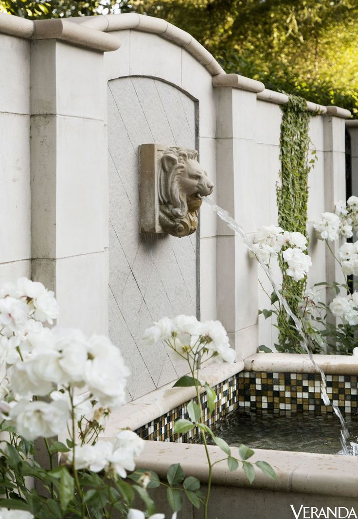 a fountain with white flowers and greenery around it