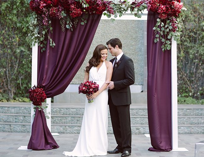 a bride and groom standing under a purple wedding arch