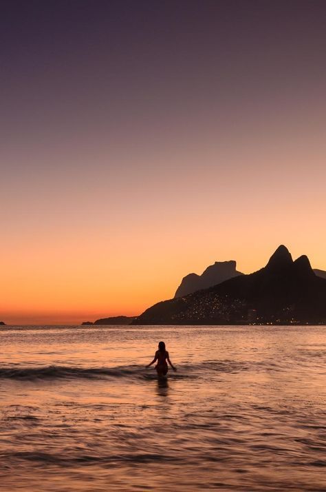 a person is wading in the water at sunset with mountains in the back ground