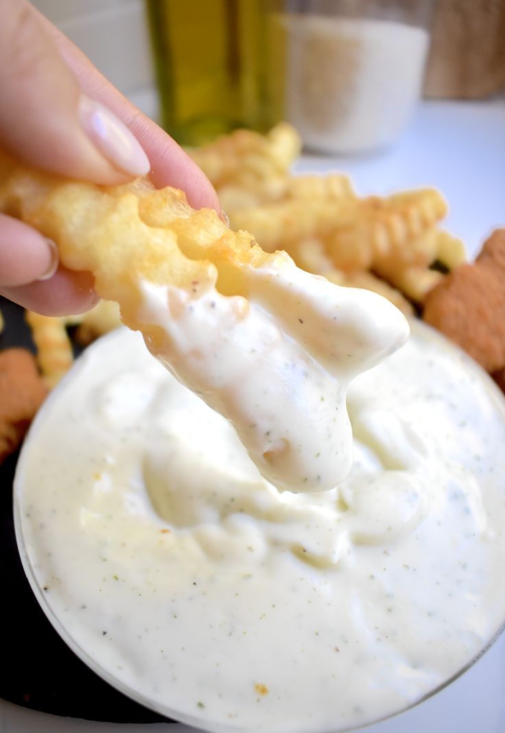 a person dipping some kind of food into a white bowl with ranch dressing on it