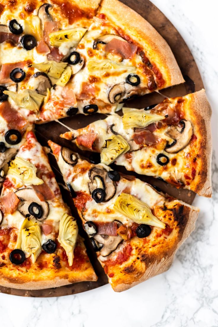 a pizza with olives, ham and cheese cut into eight slices on a wooden platter