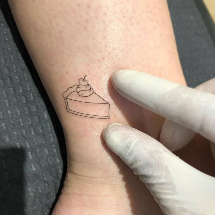 a person with a small tattoo on their arm holding up a piece of cake in front of them