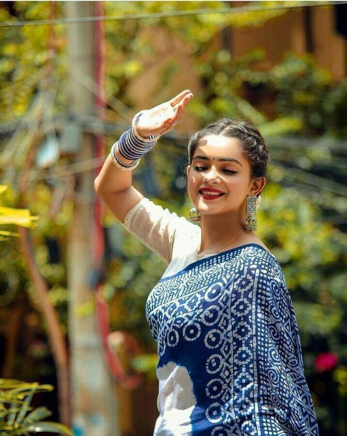 a woman in a blue and white sari waving at the camera with her hand up