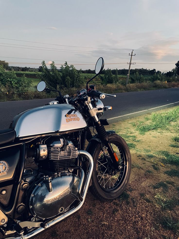 the motorcycle is parked on the side of the road in front of some grass and trees