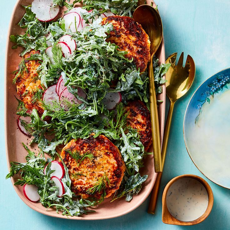 crab cakes with radishes and greens on a pink platter next to silverware