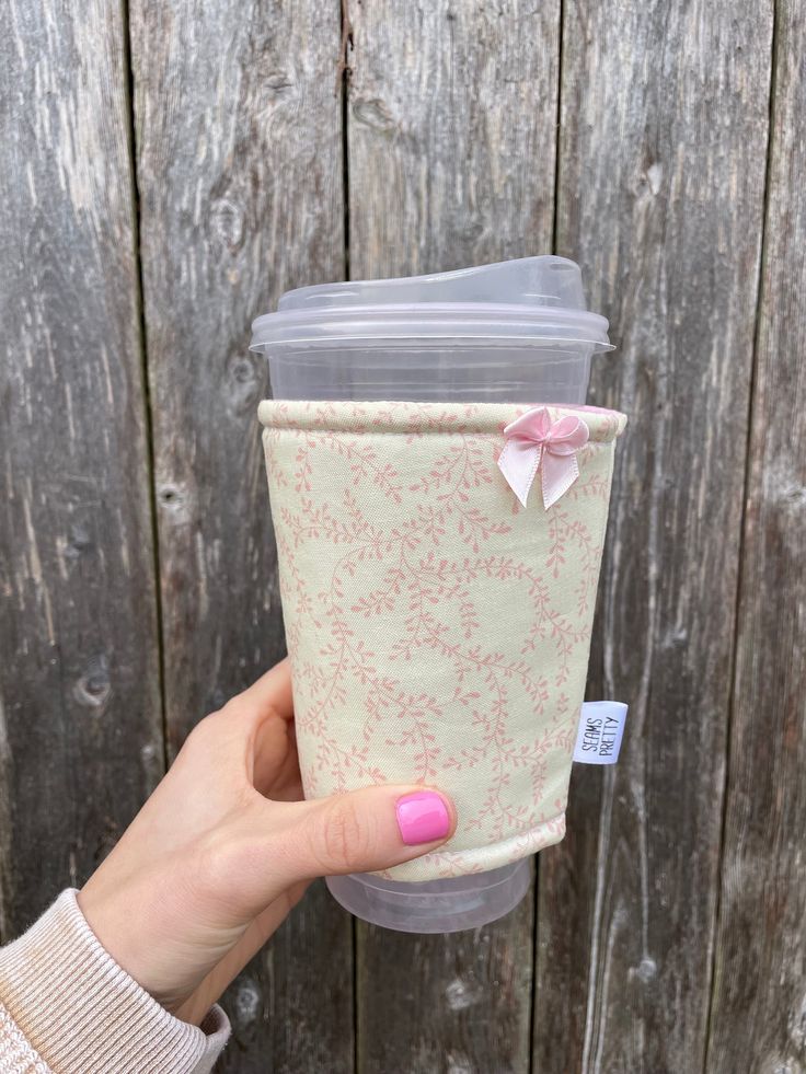 a woman holding up a cup with a pink bow on it's lid and sleeve